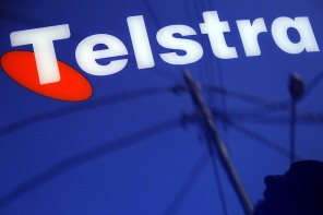 A man and power lines are reflected in a Telstra poster adorning a public telephone in Sydney, Australia