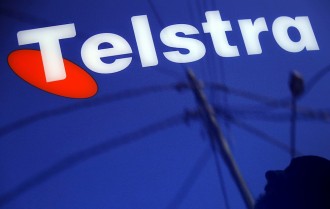A man and power lines are reflected in a Telstra poster adorning a public telephone in Sydney, Australia